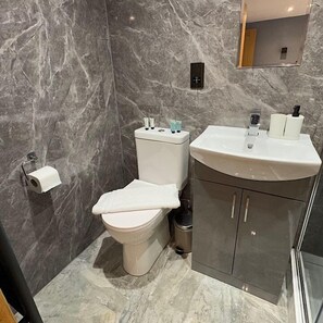 A bathroom with a toilet, sink, and marble walls. - Modern Double Studio | Near CBS Arena (Kitchenette) (West Midlands)