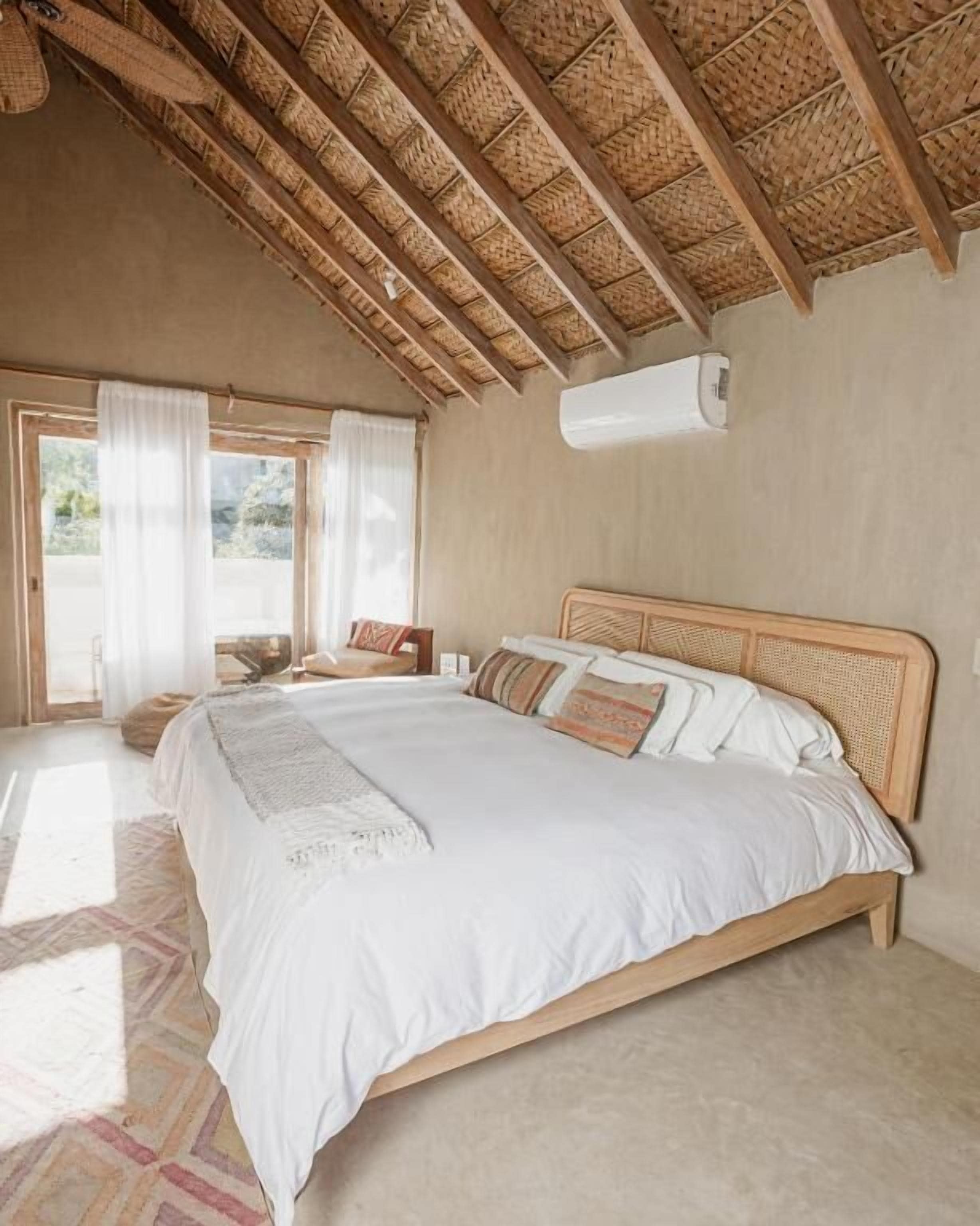 A bedroom with a large bed, a wooden ceiling, and a window with curtains.