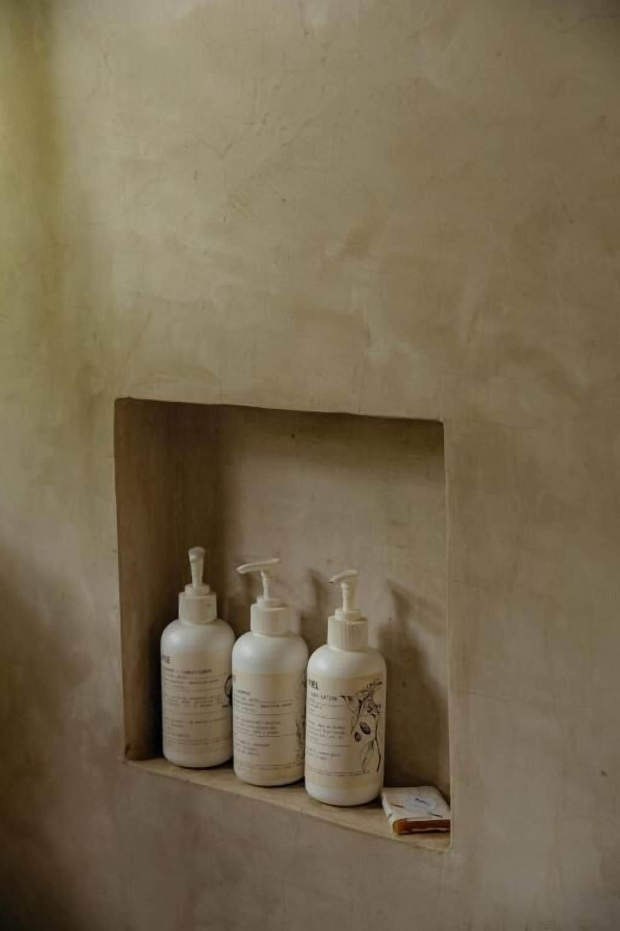 A shelf with three toiletry bottles and a small book in a textured wall alcove.