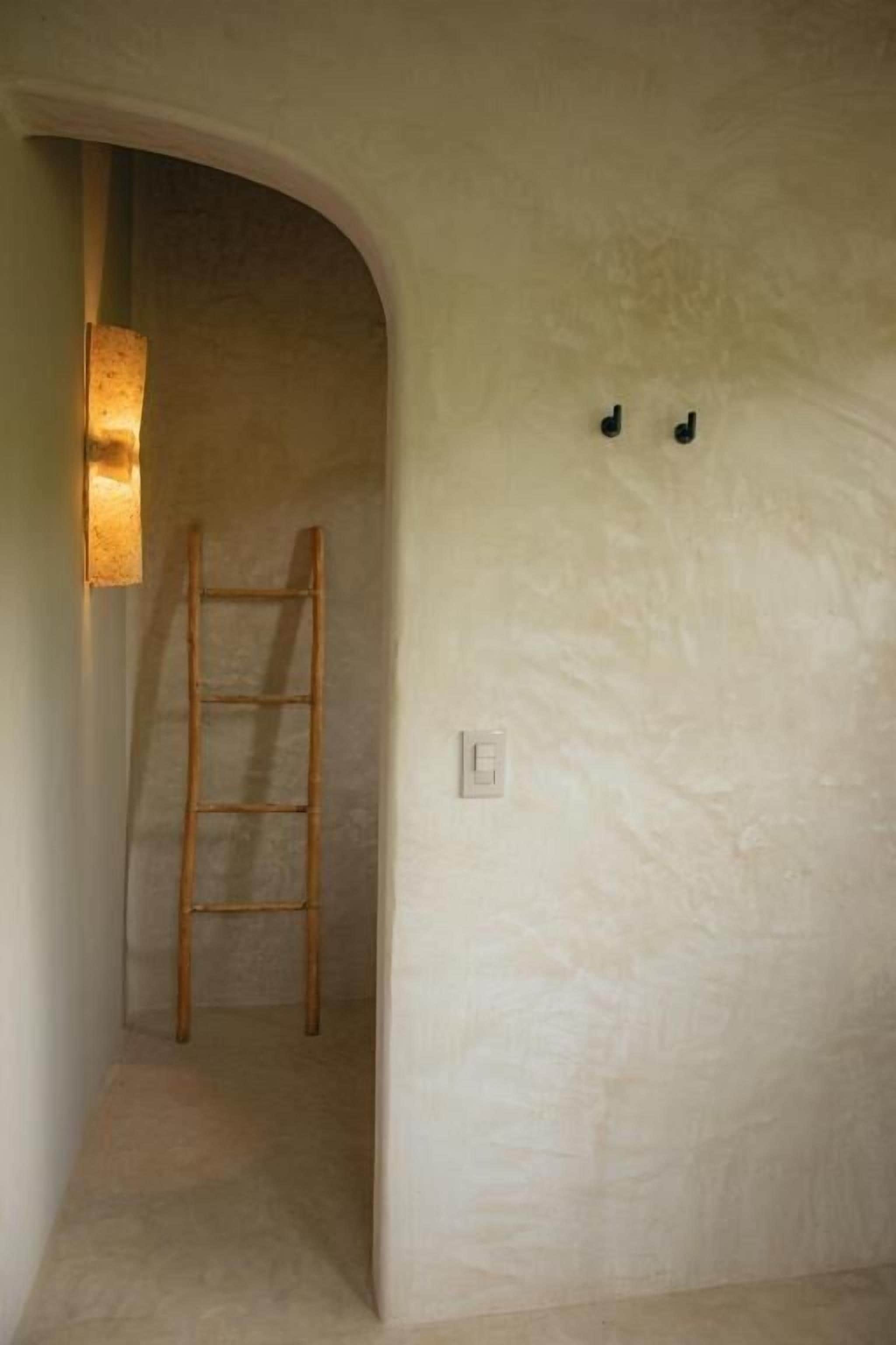 A narrow hallway with a wooden ladder leaning against the wall, a light fixture, and a switch on the wall.