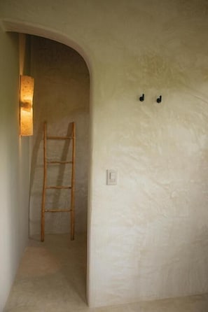 Un pasillo estrecho con una escalera de madera apoyada en la pared, una lámpara y un interruptor.