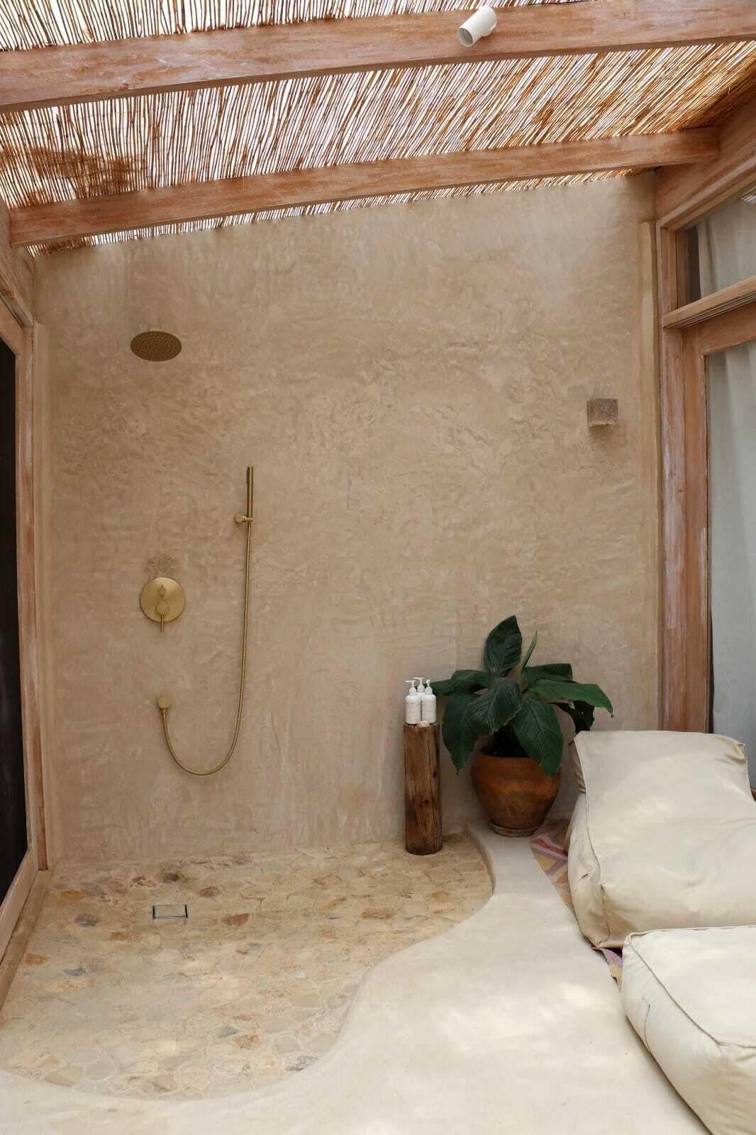 Un área de ducha al aire libre con techo, suelo de piedra, banco de madera y planta en maceta.