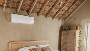 Un dormitorio con cama de madera, cabecera tejida, armario de fibra natural y una planta en maceta.