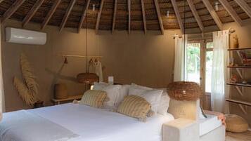 Un dormitorio con cama, almohadas, una lámpara colgante y un ventanal con cortinas.