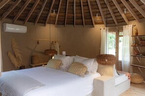 Un dormitorio con cama, almohadas, una lámpara colgante y un ventanal con cortinas.