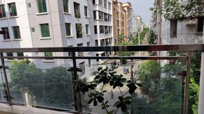 A view from a balcony with a metal railing, overlooking a street with multi-story buildings, some with balconies and greenery. - Stunning Apt in Secured Area (Dhaka)