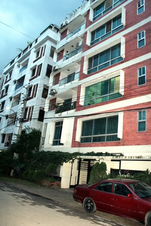 A multi-story building with balconies, large windows, and a red car parked in front. - Stunning Apt in Secured Area (Dhaka)