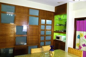 A room with a dining table, chairs, a microwave, and a green shelf with various items. - Stunning Apt in Secured Area (Dhaka)