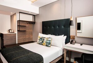 Une chambre d’hôtel moderne équipée d’un lit, d’une table de chevet, d’un bureau et d’une armoire intégrée.