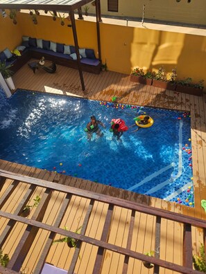 A swimming pool with a wooden deck, a seating area with cushions, and potted plants. - Premium Luxury Villa – Perfect for Families & Groups (Maputo)
