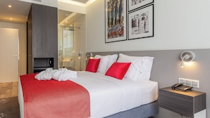 Une chambre d’hôtel moderne avec un grand lit, une table de chevet avec une lampe et des œuvres d’art accrochées au mur.