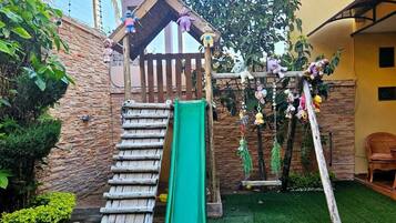 Un espace de jeux pour enfants avec un toboggan, une structure d’escalade et un petit pavillon.