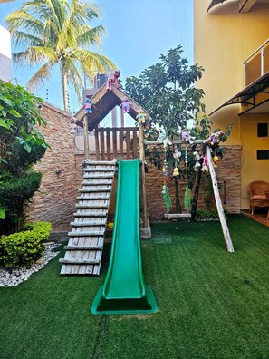 Un espace de jeux pour enfants avec un toboggan, une structure d’escalade et un petit pavillon.