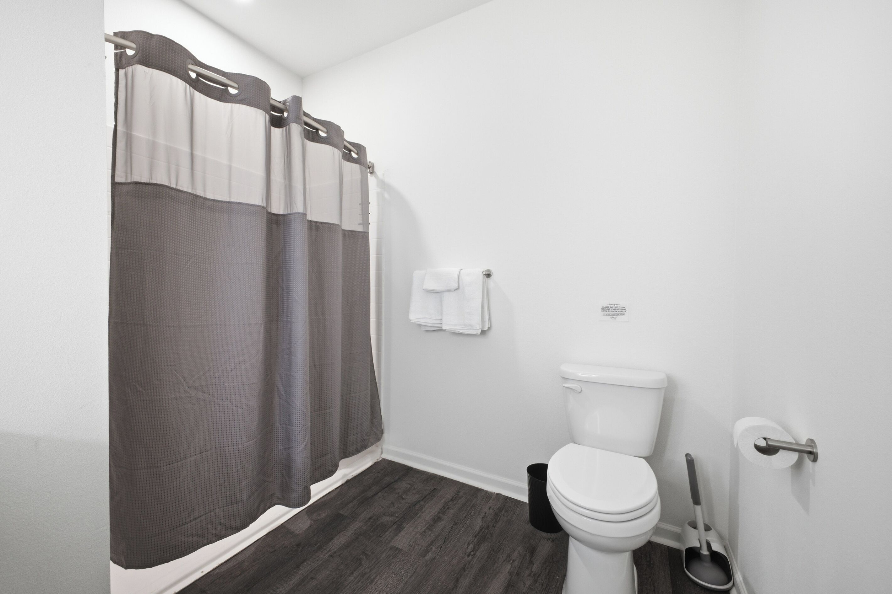 A bathroom with a toilet, a shower curtain, a towel rack, and a floor mat.