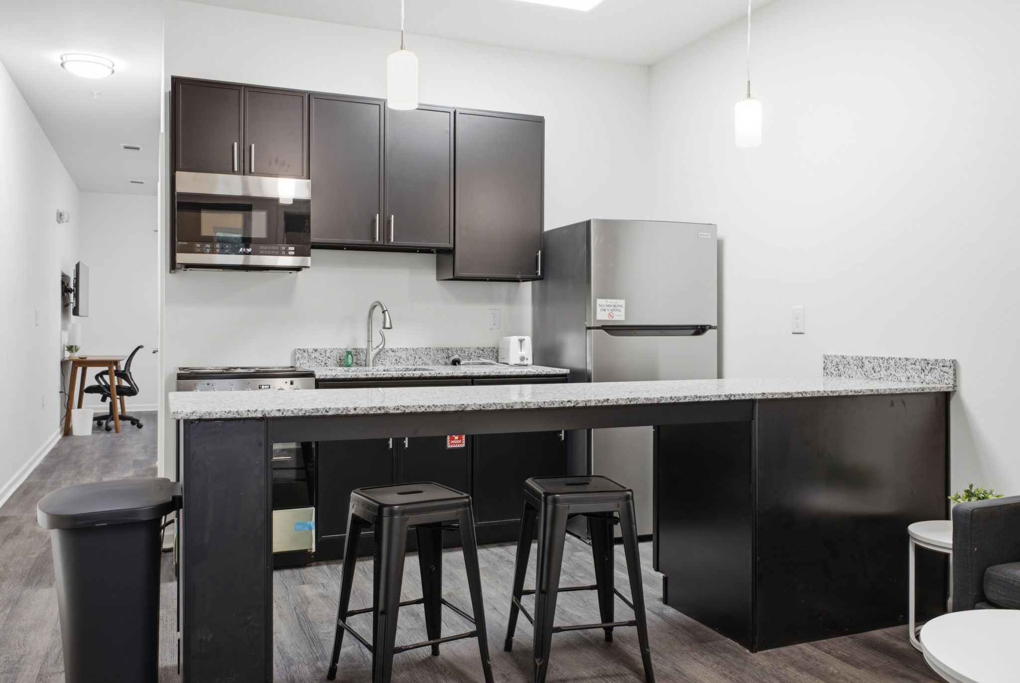 A modern kitchen with dark cabinetry, a stainless steel refrigerator, a built-in oven, and a granite countertop.