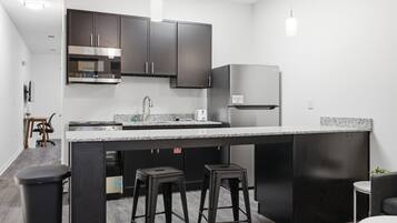 A modern kitchen with dark cabinetry, a stainless steel refrigerator, a built-in oven, and a granite countertop.
