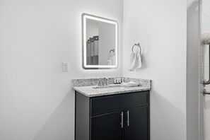 A modern bathroom with a granite countertop, a black cabinet, a wall-mounted mirror, and a towel rack.