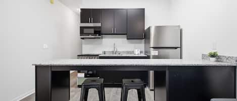 Cocina moderna con una isla central, gabinetes negros y electrodomésticos de acero inoxidable, y dos taburetes.