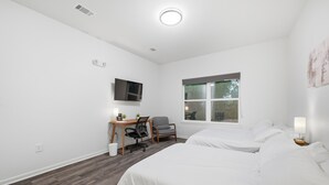 Een hotelkamer met twee bedden, een bureau met stoel, een televisie en een raam.