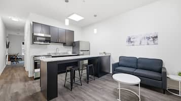 A modern kitchen with a central island, bar stools, and a grey sofa in a living area.