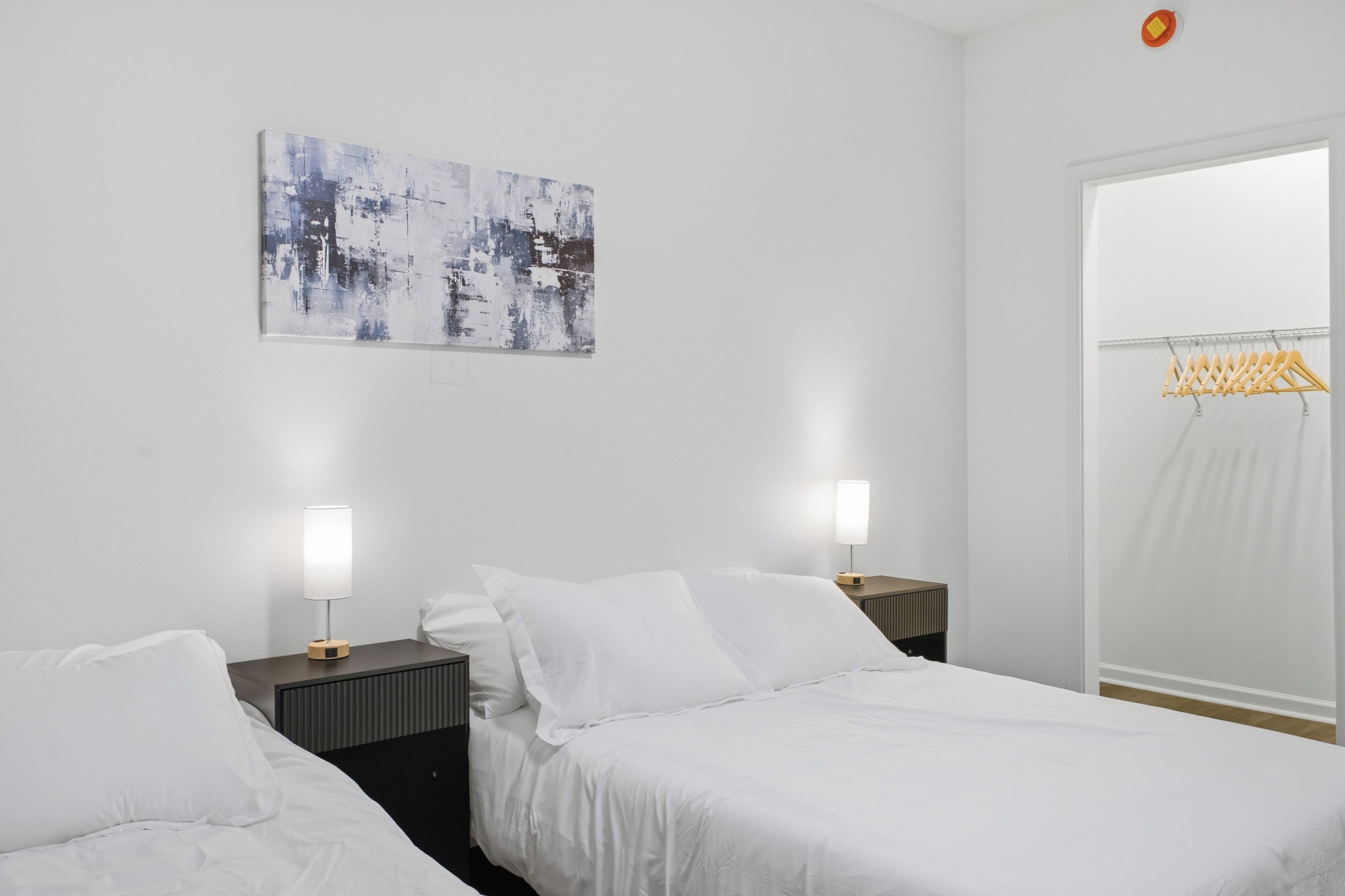 Una habitación de hotel con dos camas, una obra de arte colgada en la pared, una ventana con cortina y un perchero.