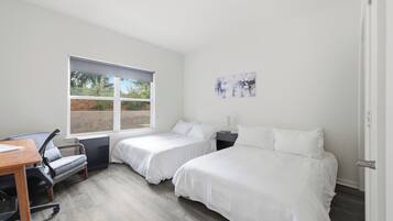 A bedroom with two beds, a desk, and a chair.