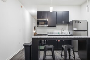 Una cocina moderna con armarios oscuros, un refrigerador de acero inoxidable y una encimera de granito.