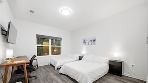 Een hotelkamer met twee bedden, een bureau, een stoel, een raam met uitzicht op bomen, en een schilderij aan de muur.