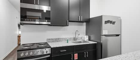 Une cuisine compacte équipée d’une cuisinière à gaz, d’un four, d’un réfrigérateur en acier inoxydable et de meubles de cuisine noirs.