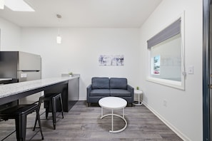 Et kompakt køkken med indbygget køleskab, en bardisk og en grå sofa.