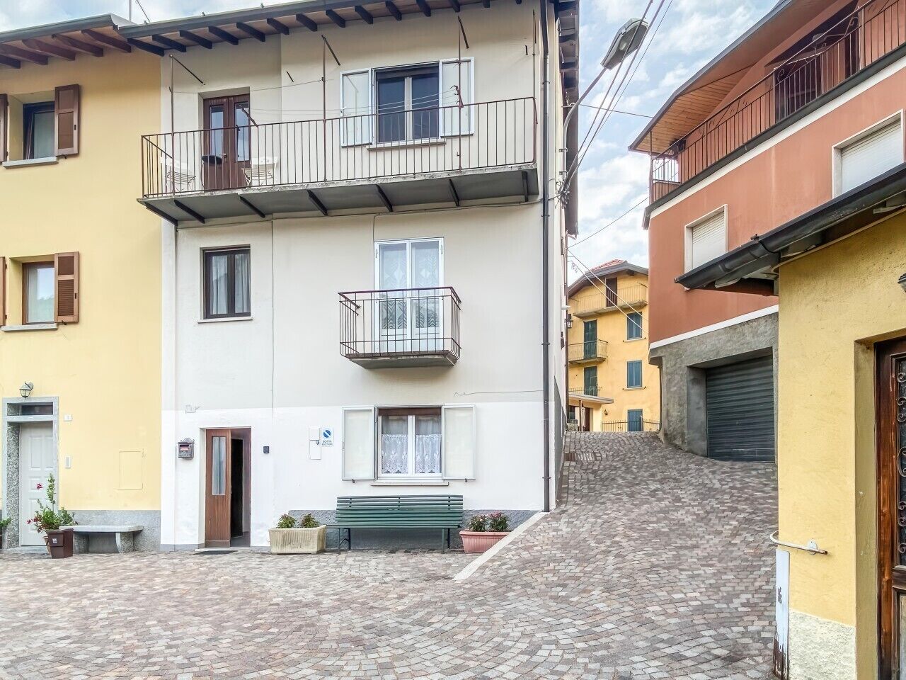 Eine schmale Straße mit Gebäuden an beiden Seiten, einer Bank und einer kleinen Treppe zu einer höheren Ebene.
