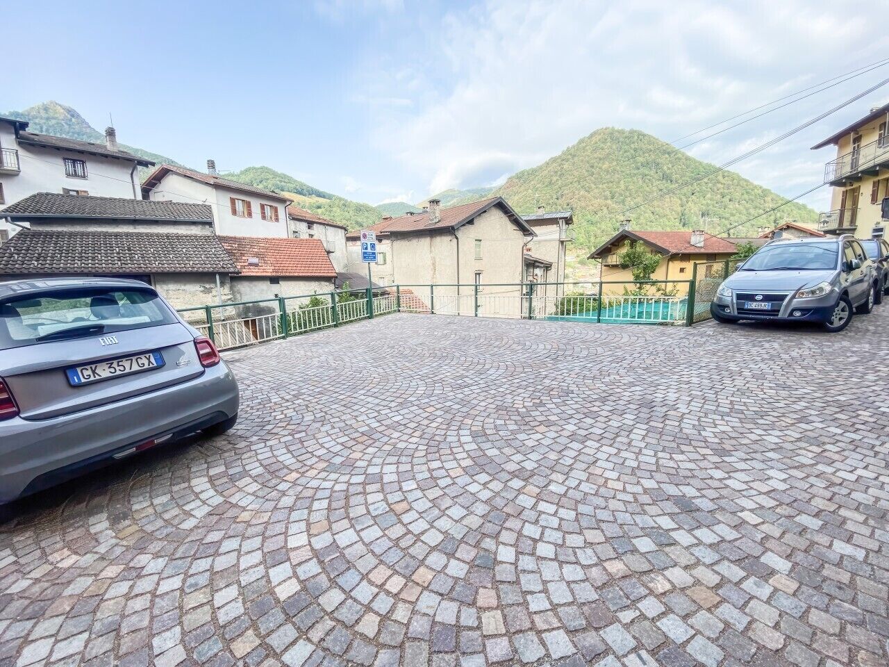 Une cour pavée où est garée une voiture, sur le côté gauche, et qui est entourée de bâtiments à l’architecture traditionnelle.