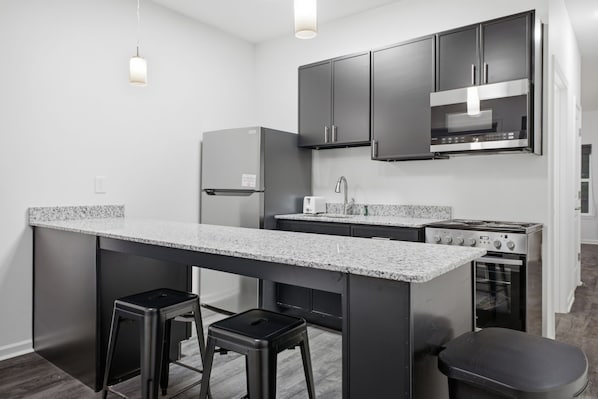 Una cocina moderna con una isla central, taburetes de bar, horno empotrado y electrodomésticos de acero inoxidable.