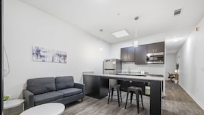 Eine moderne Küche mit grauem Sofa, einem kleinen Esstisch und einer Bar mit Hockern.