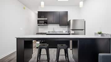 A modern kitchen with a central island, black cabinets, stainless steel appliances, and two stools.