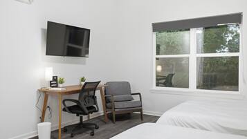 A hotel room with a bed, a desk with a chair, a television, and a window with a view of trees.