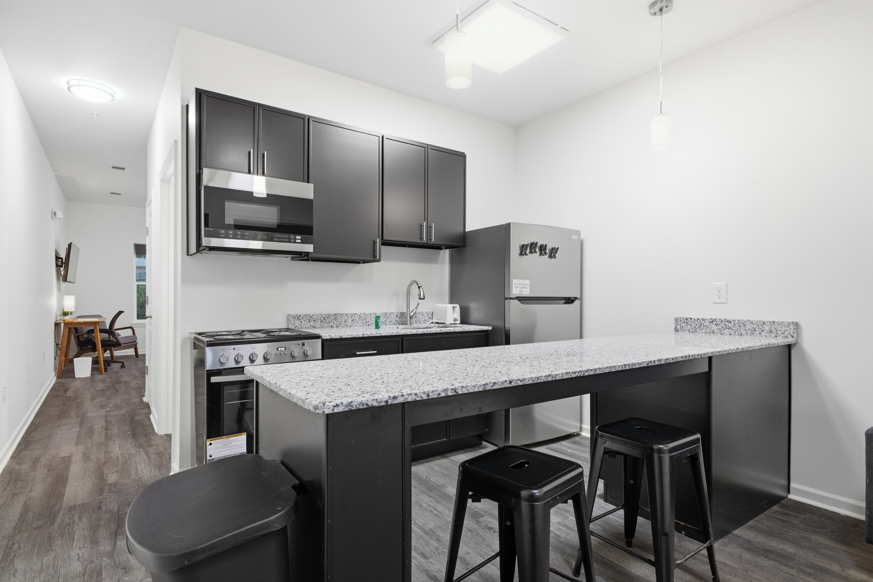 A modern kitchen with stainless steel appliances, a granite countertop, and black bar stools.