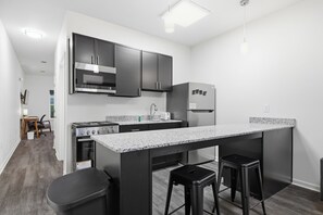Una cocina moderna con electrodomésticos de acero inoxidable, encimera de granito y taburetes negros.