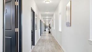 Un pasillo con piso de color claro, paredes blancas y puertas a ambos lados.