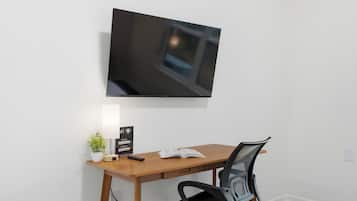 A room with a wooden desk, a chair, a television mounted on the wall, a small potted plant, a remote control, and a sign with network information.