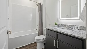 Un baño con una bañera blanca, inodoro, tocador con lavamanos y espejo.