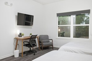 Et hotelværelse med en seng, et skrivebord med stol, et fjernsyn og et vindue med udsigt til træer.