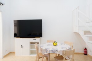 A room with a flat-screen TV mounted on a white cabinet, a round table with a white tablecloth, and a wooden chair. - La Marina (Sorrento)