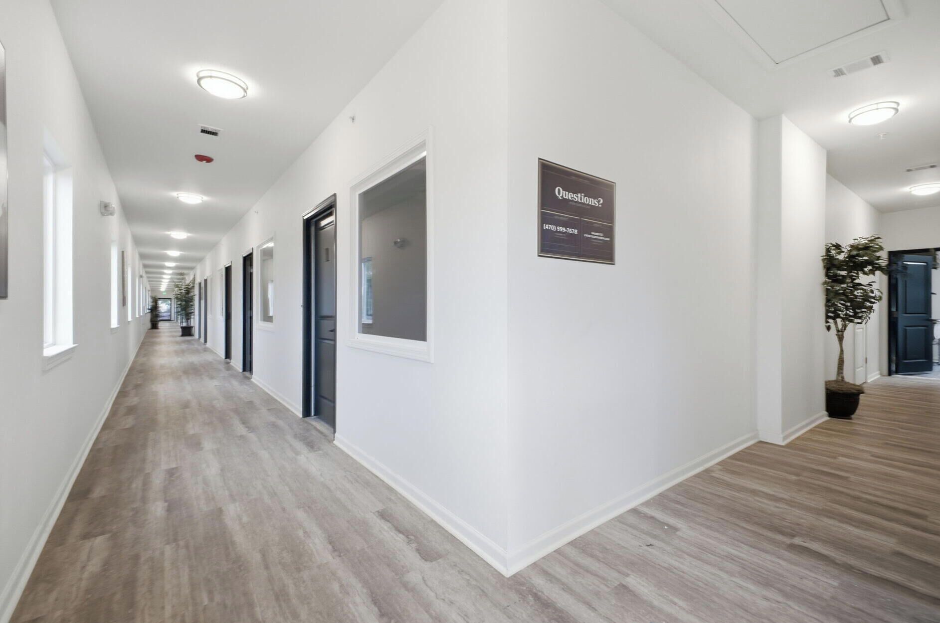 Un couloir d’hôtel avec un panneau indicateur, des portes et une plante en pot.
