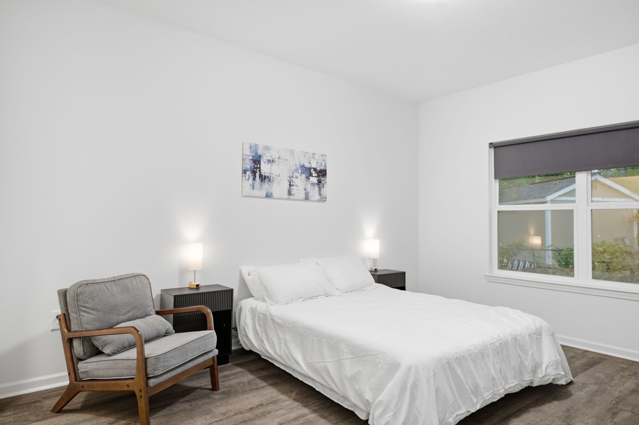 Une chambre à coucher comprenant un lit, une chaise, des tables de chevet, une œuvre d’art murale et une fenêtre.