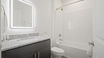 A bathroom with a vanity, sink, mirror, toilet, and shower area.