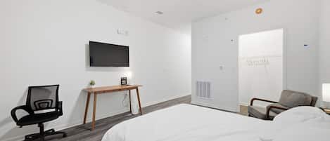 Una habitación de hotel con cama, escritorio, silla, televisor y armario.