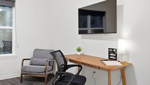 Habitación de hotel con escritorio de madera, una silla, televisor montado en la pared, una planta pequeña sobre el escritorio y un cartel de Wi-Fi.