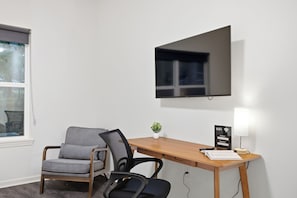 A hotel room with a wooden desk, a chair, a television mounted on the wall, a small plant on the desk, and a Wi-Fi sign.