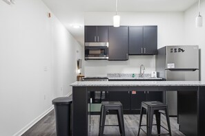 Una cocina moderna con armarios oscuros, un refrigerador de acero inoxidable, horno empotrado y encimera de granito.